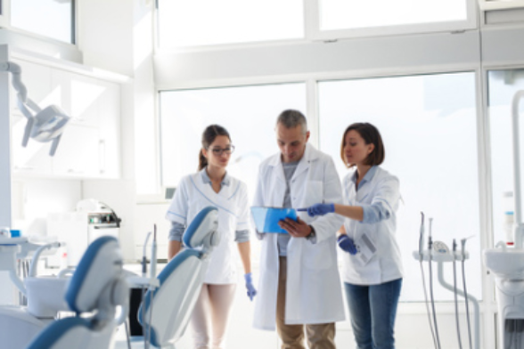 Tre persone in camice bianco consultano una cartella in uno studio dentistico.